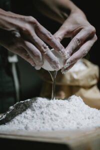 cook adding egg to heap of dough scattered on table