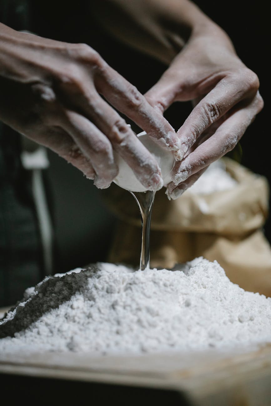 cook adding egg to heap of dough scattered on table